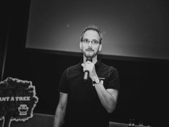 Jan Fischbach mit Mikrofon in der Hand beim Scrum-Day. Im Hintergrund ein Aufsteller zum Scrumwald (www.scrumwald.de)